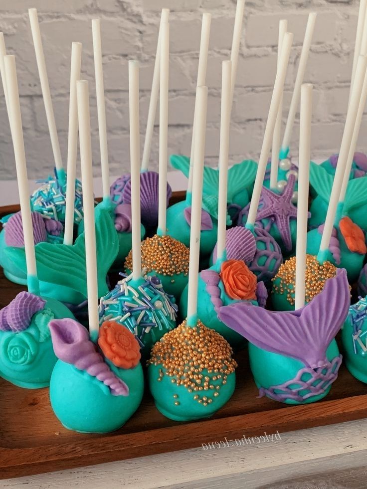 Colorful mermaid-themed cake pops with teal and purple decorations, featuring seashells, mermaid tails, and sprinkles.