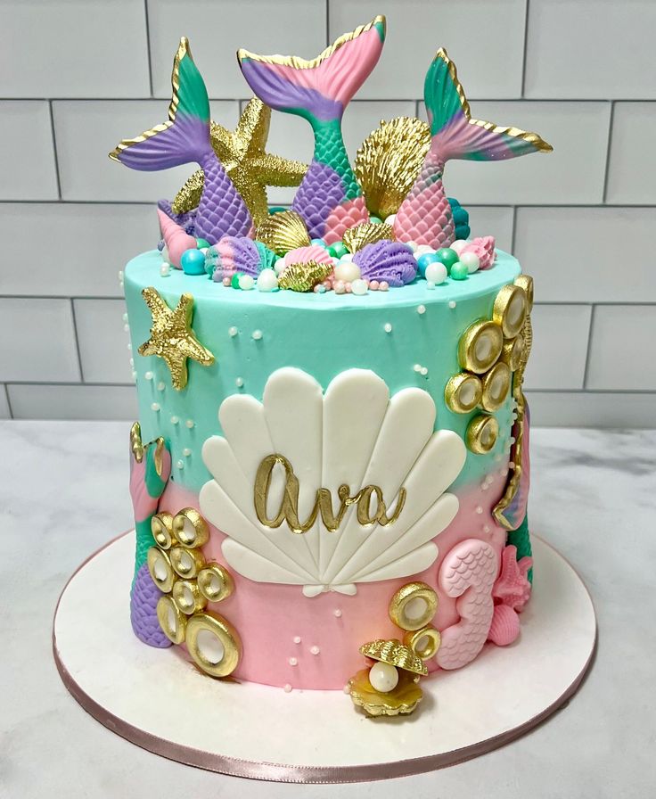 A stunning cake with a pink and turquoise gradient, highlighted by golden accents like mermaid tails, coins, and shells. It exudes elegance and vibrancy, perfect for a chic undersea celebration